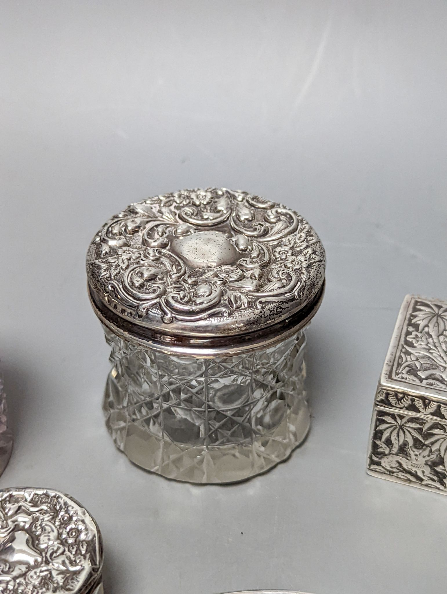 A silver mounted hand mirror, five assorted silver mounted glass toilet jars and an Indian white metal rectangular box.
